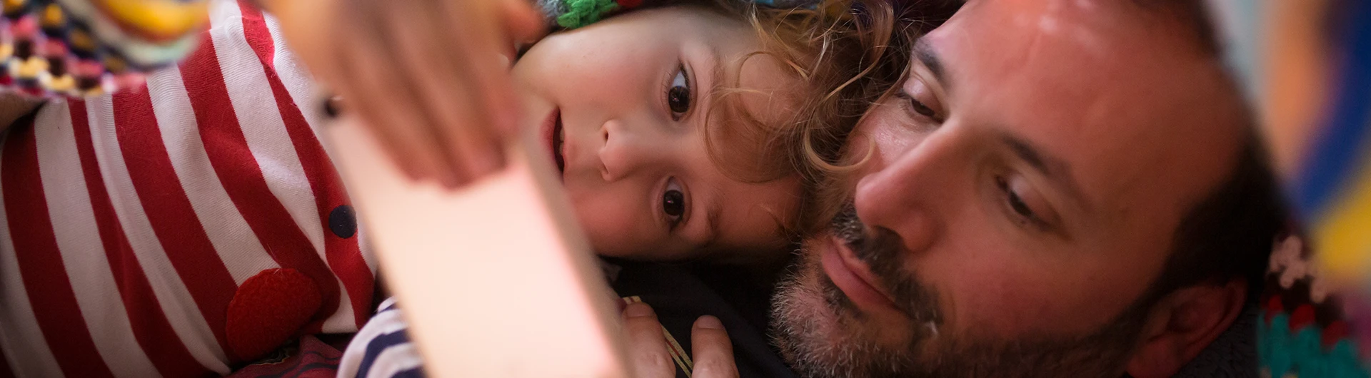 Father and daughter under a blanket watching something on the phone (photo)