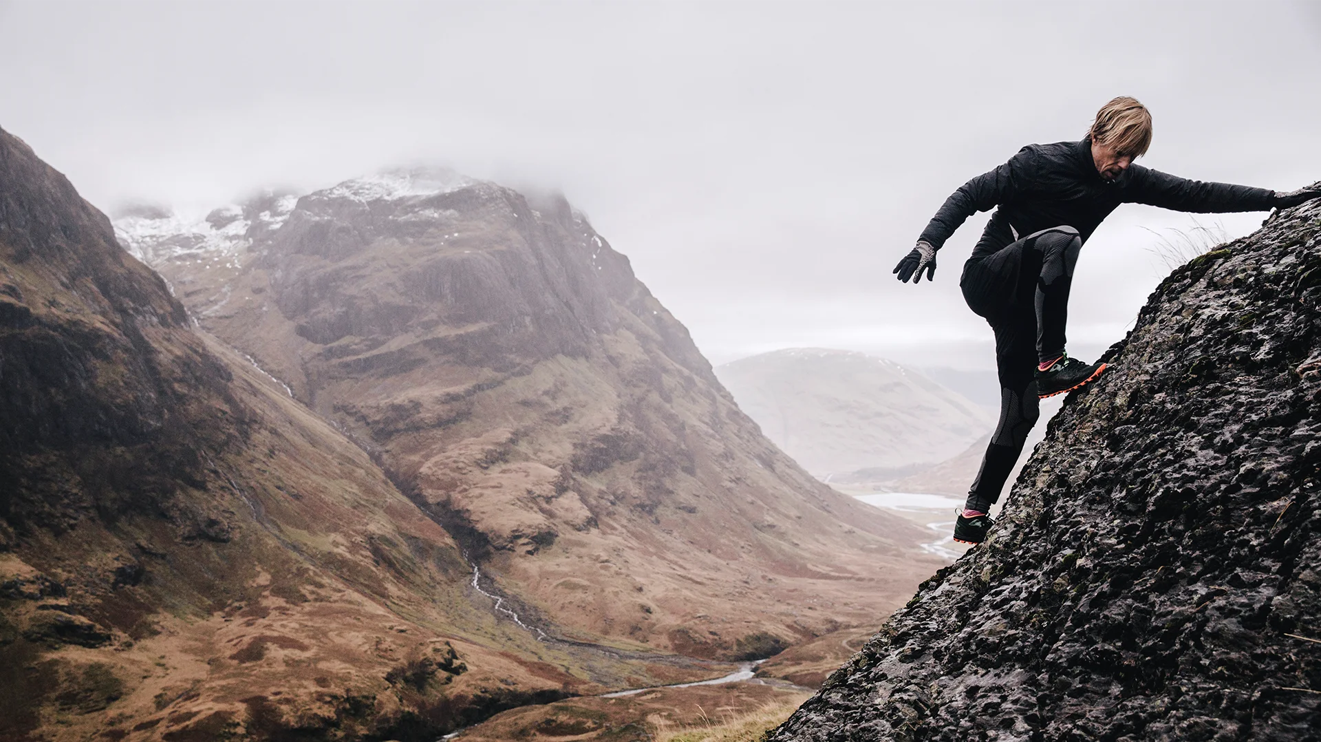 Man climbing a rock with foggy mountain view in the background (photo)