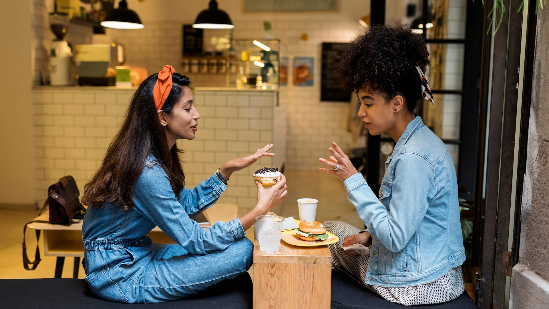 Two woman sitting in a coffee shop, drinking coffee and talking (photo)