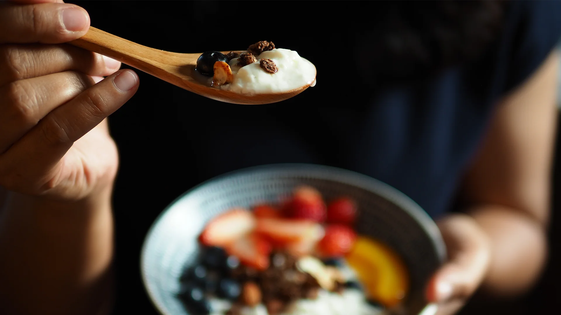 Person holding a porridge bowl and a spoon with porridge and fruits (photo)