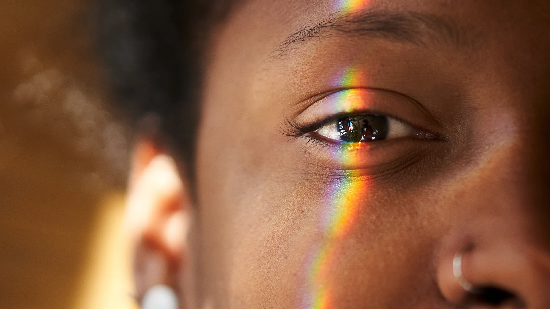 Person looking in the camera with the reflection of a rainbow on their face (photo)