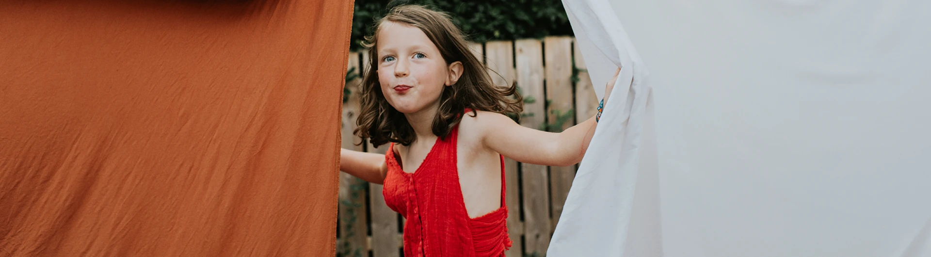 Girl in a red dress inbetween curtains (photo)
