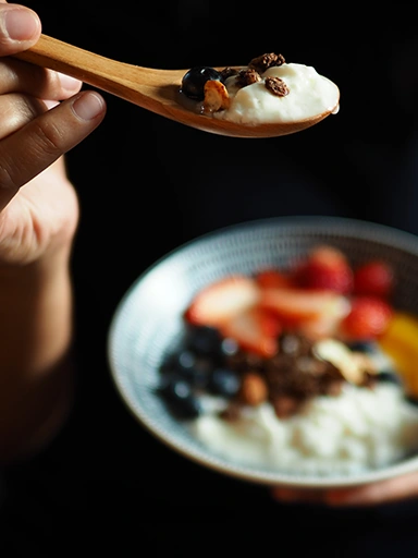 Person holding a porridge bowl and a spoon with porridge and fruits (photo)