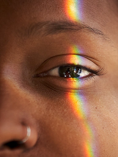 Person looking in the camera with the reflection of a rainbow on their face (photo)