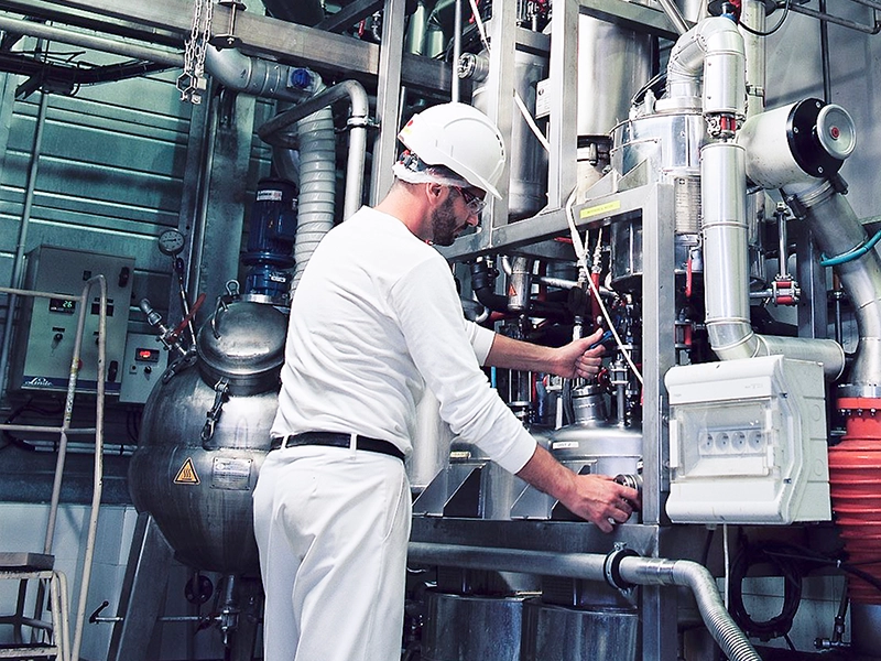 A factory worker wearing a helmet and protective glasses operates industrial machinery and controls inside a production facility. (photo)