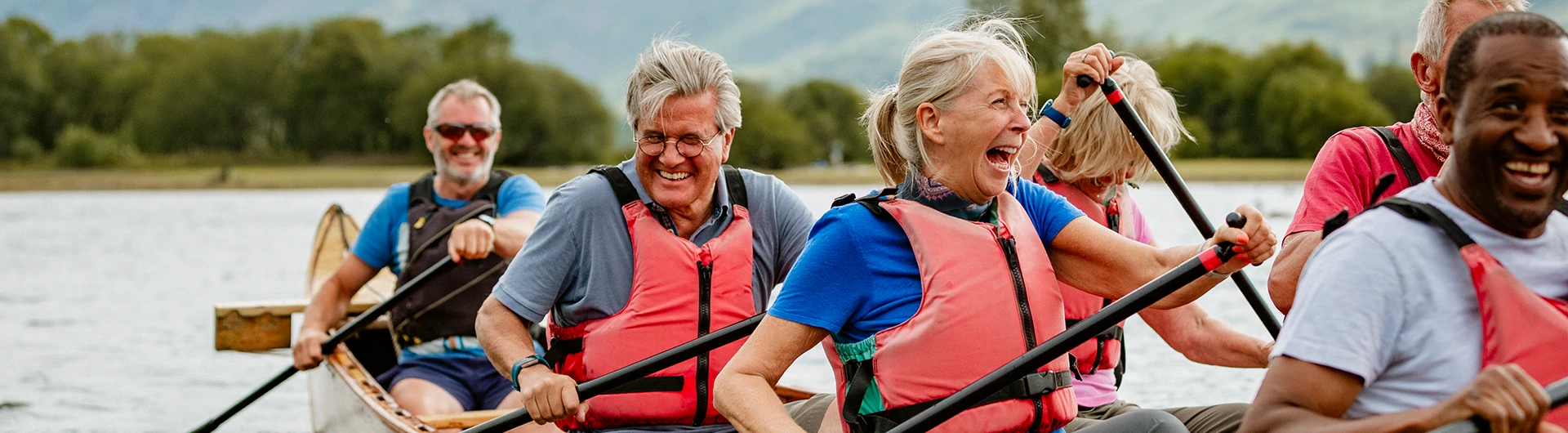 A group of older adults paddle a canoe together on a lake, laughing and enjoying the activity. (photo)