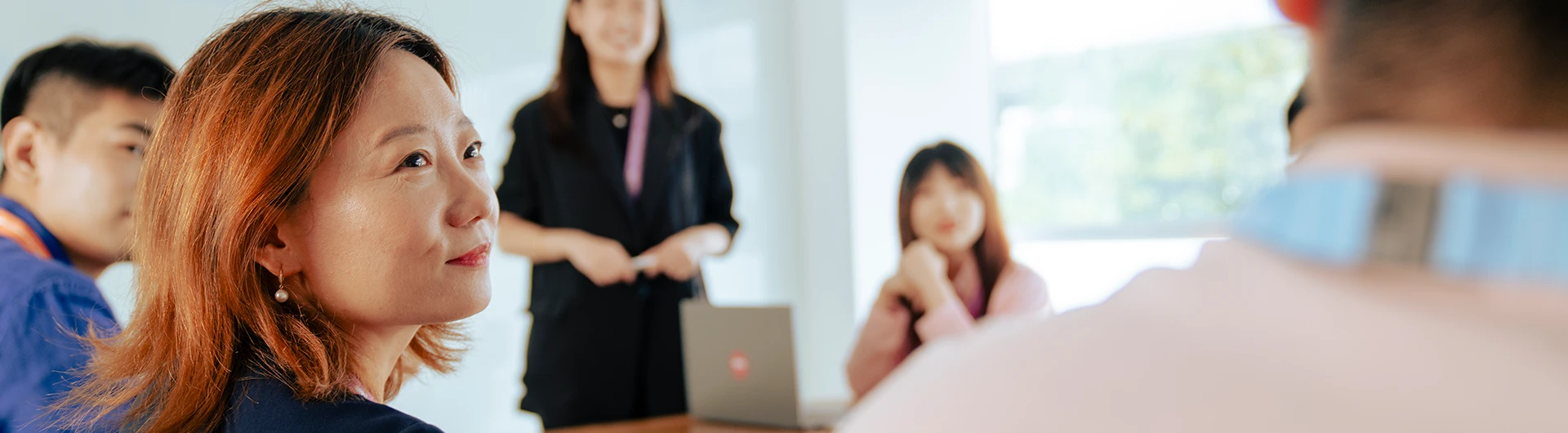 A woman listening attentively during a meeting, with colleagues in the background. (photo)