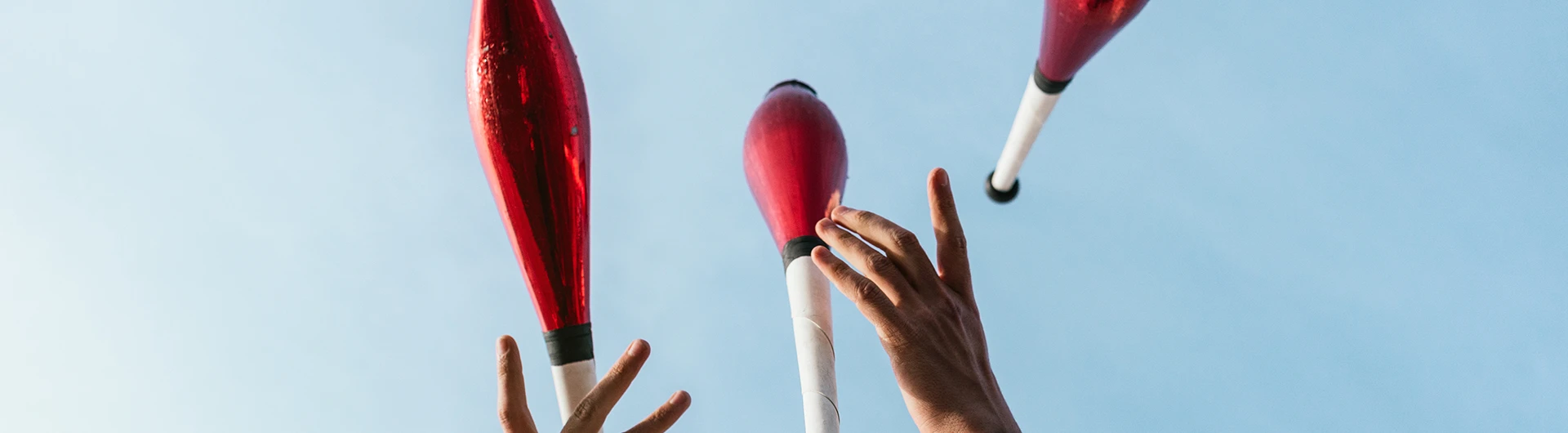 Hands tossing juggling clubs into the air against a clear blue sky. (photo)