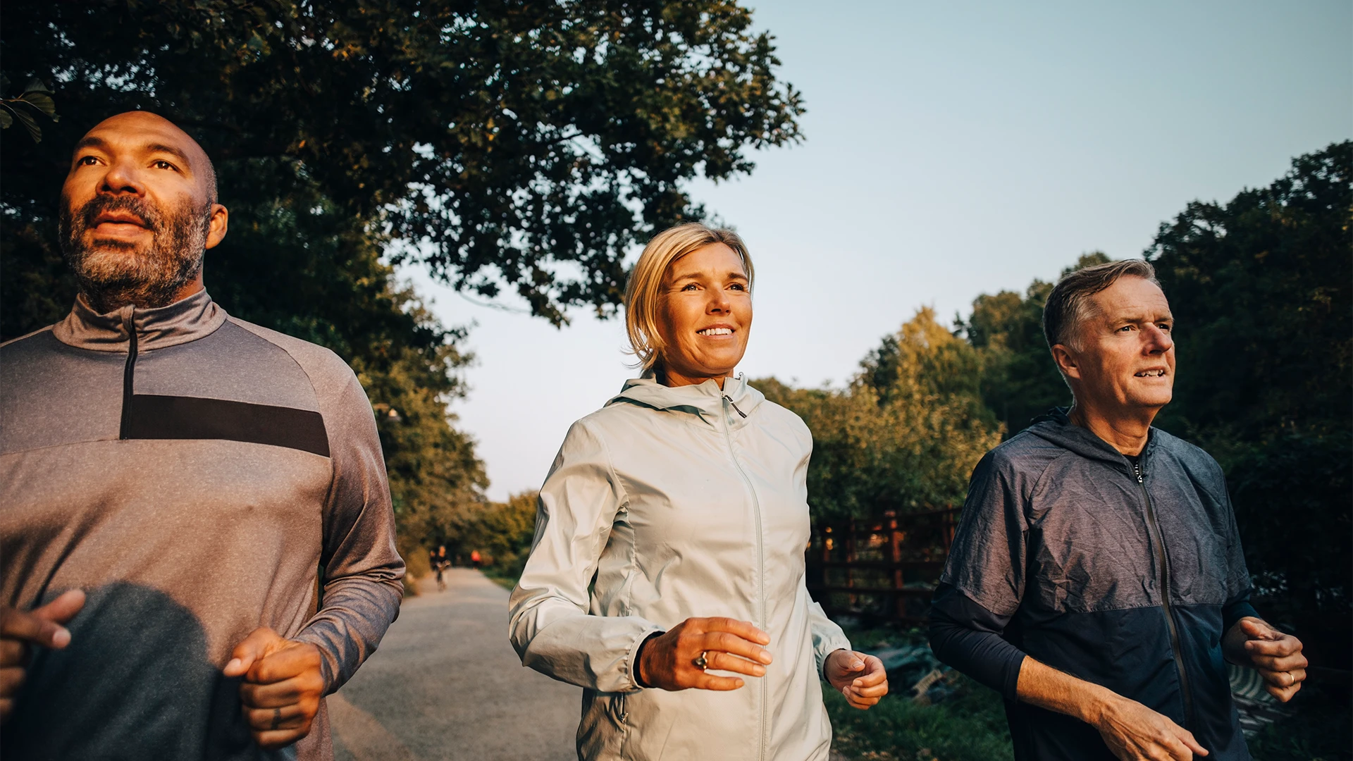 Three adults jog together along a tree-lined path in the early morning light. (photo)