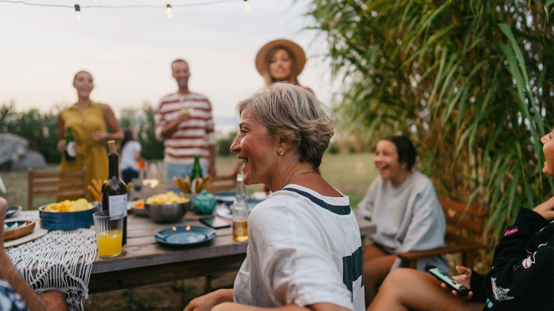 A group of friends gather around an outdoor table, laughing and enjoying a relaxed meal together in a garden setting. (photo)