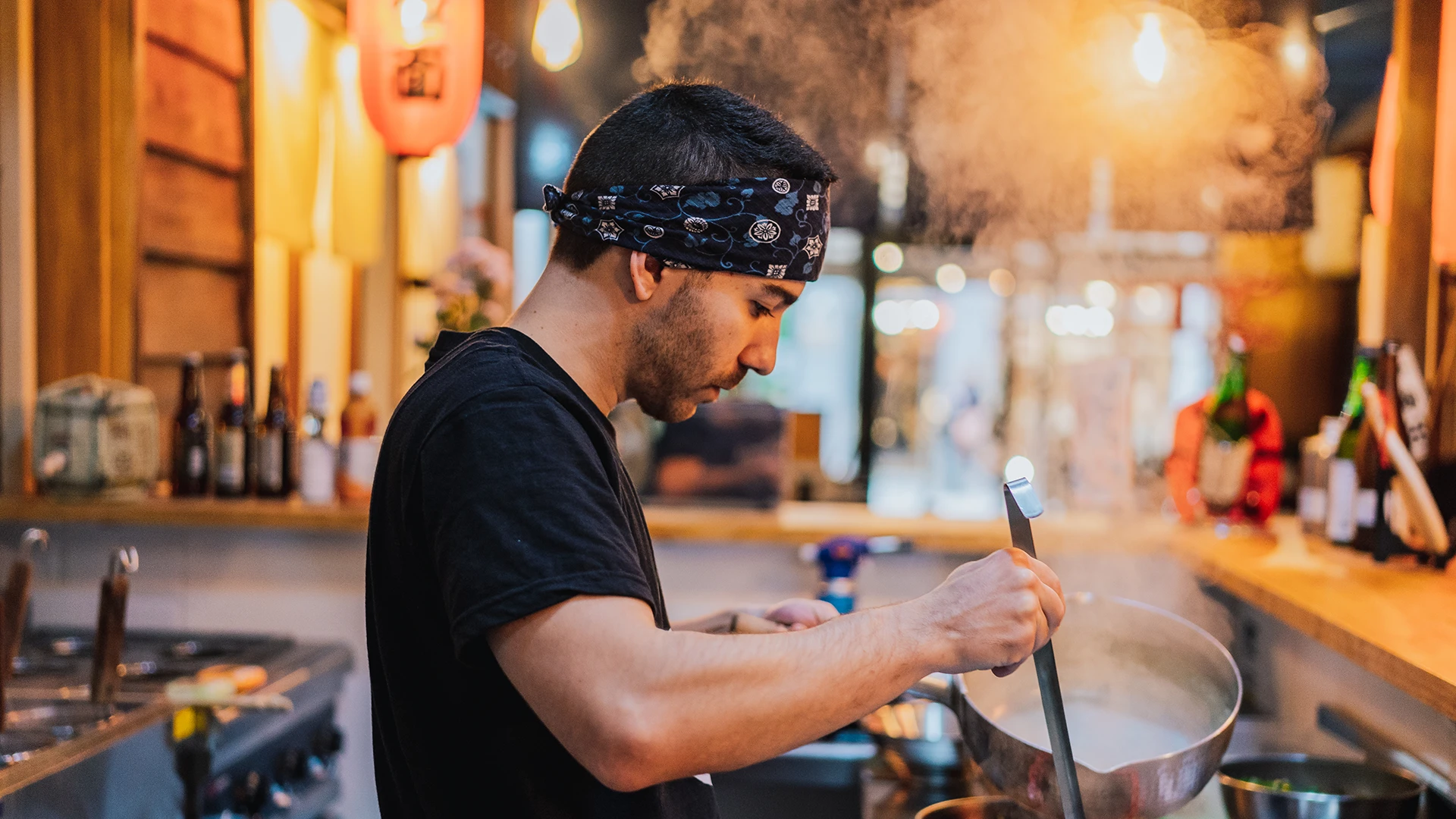 A chef stirs a steaming pot in a warmly lit restaurant kitchen. (photo)