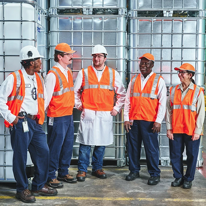 Five factory workers in safety vests and helmets standing together in front of storage tanks. (photo)