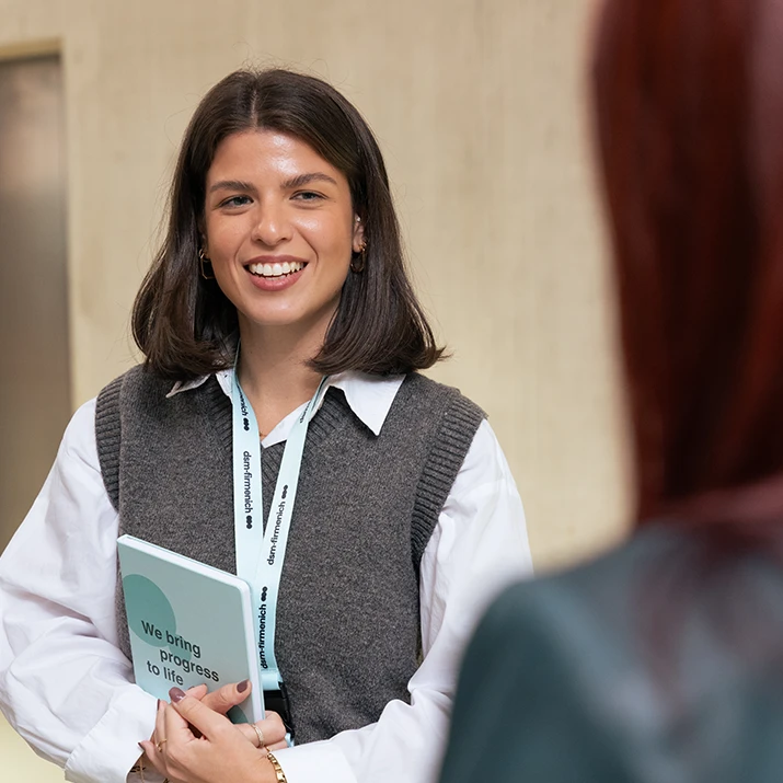 Smiling employee holding a notebook while talking to a colleague. (photo)